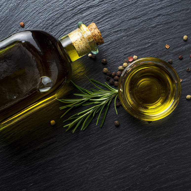 Bottle of olive oil with a sprig of rosemary and peppercorns on dark slate