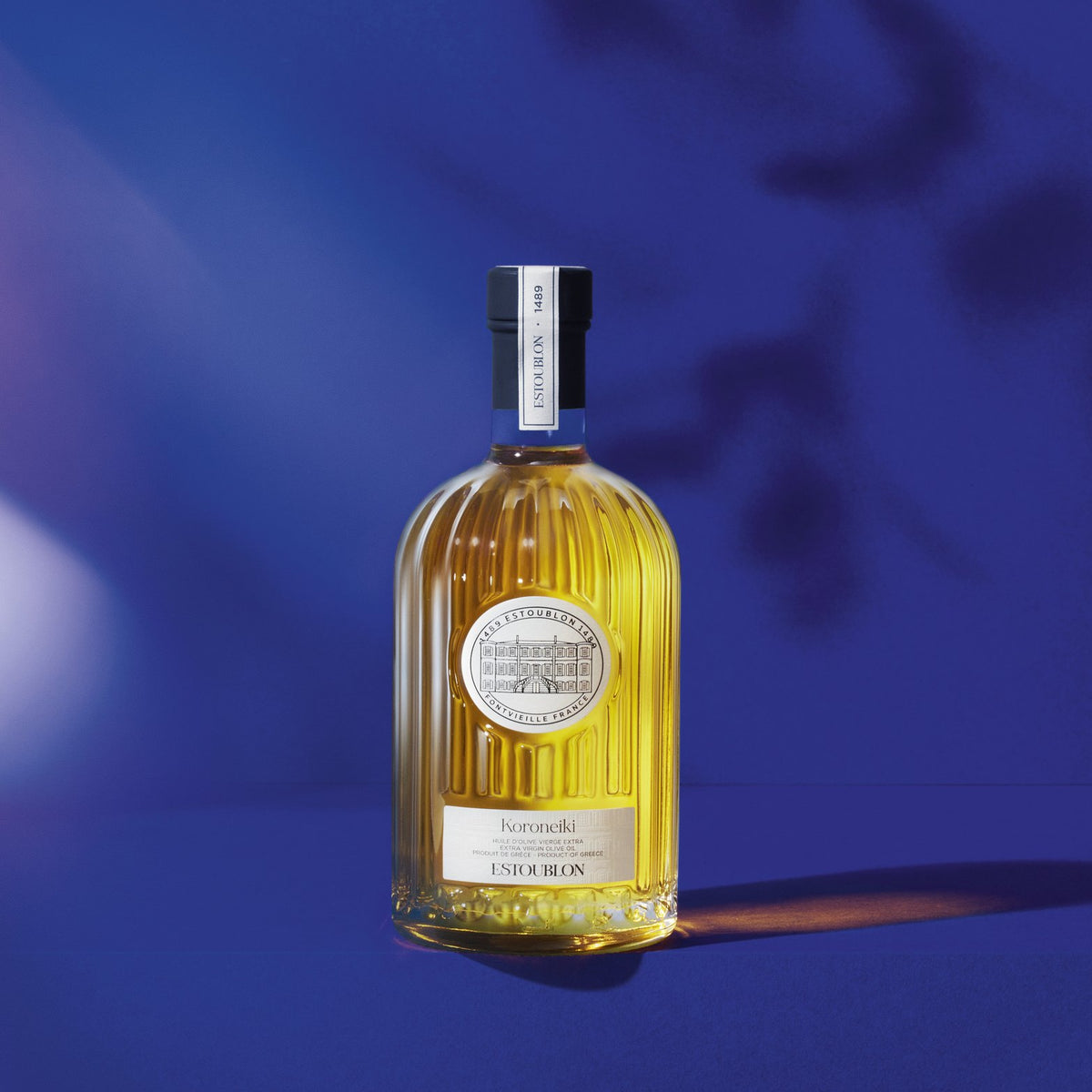 Koroneiki single-variety olive oil by Château d'Estoublon, styled on a blue background